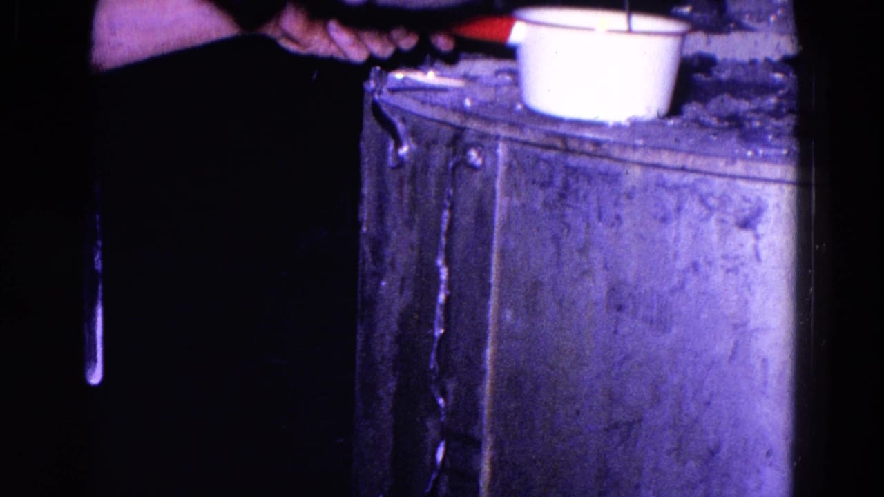 A hand holds a utensil over a white cup or small pot on a metal stove surface.