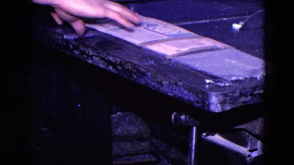 A close 8mm frame shows a hand arranging papers on a worn bench or case surface inside the 1967 Trenton private interior.