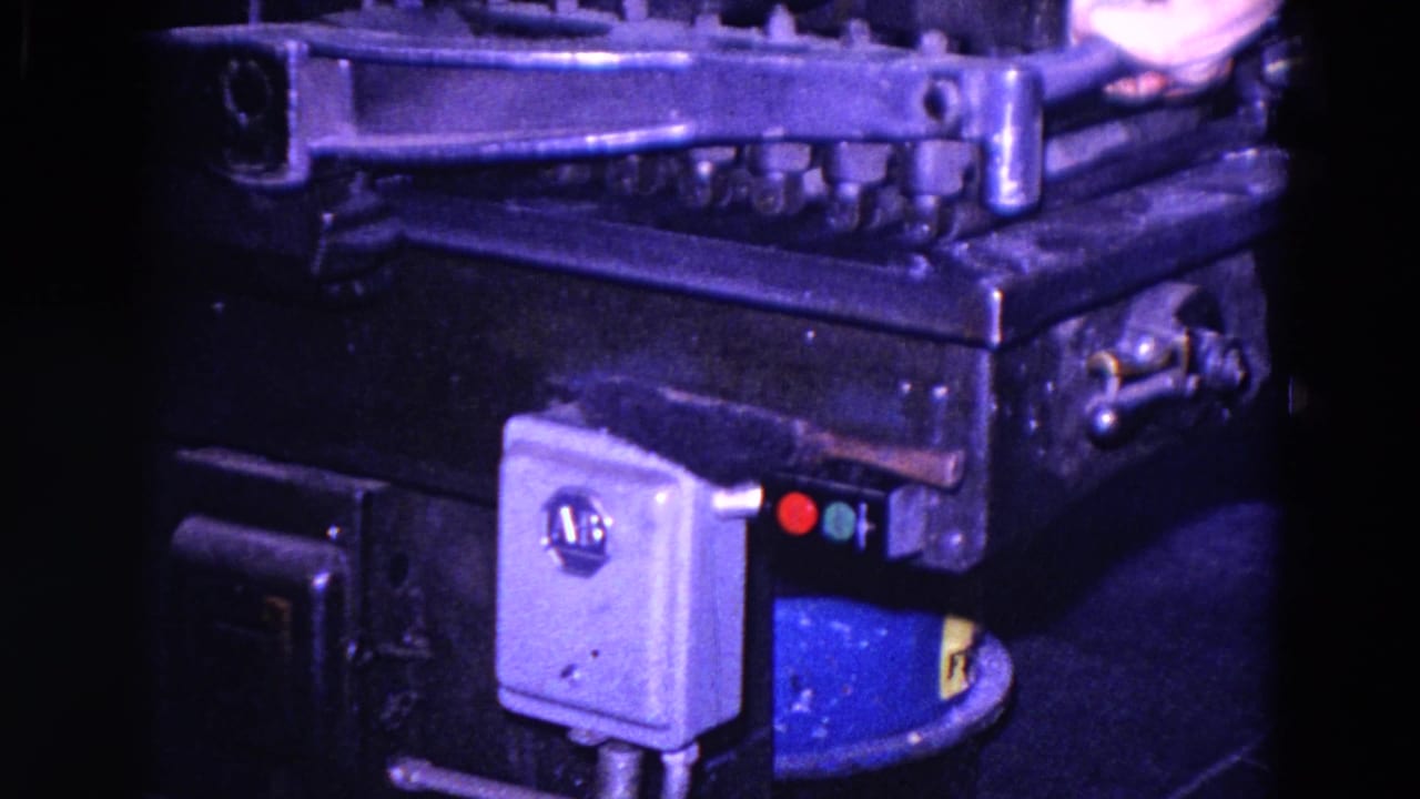 Close-up of a dark riveted machine with a small control box and colored indicator lights.