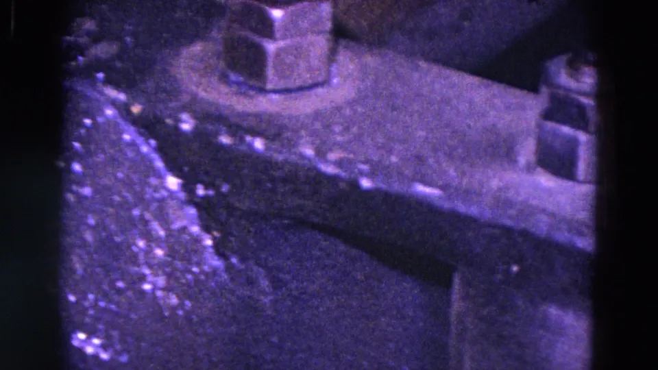 Close-up 8mm view of industrial machinery in Trenton, 1967, with a large bolt, angled metal plate, and scratched worn surface.