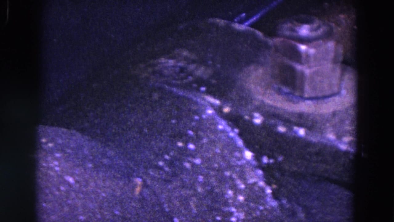 1967 Trenton 8mm frame showing a close-up of a dark tabletop or machine surface with small metal details under purple-blue lighting.