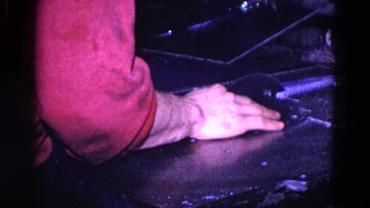 Forearm in a red sleeve and hand resting on a dark surface beside typewriter parts.