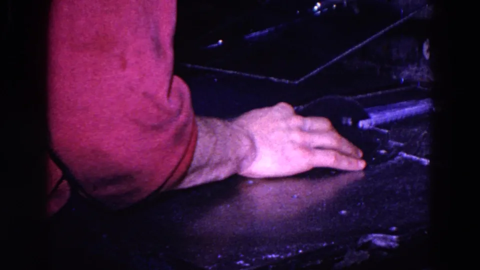 1967 Trenton 8mm frame with a red-sleeved arm and hand on a dark work surface near typewriter-related hardware.
