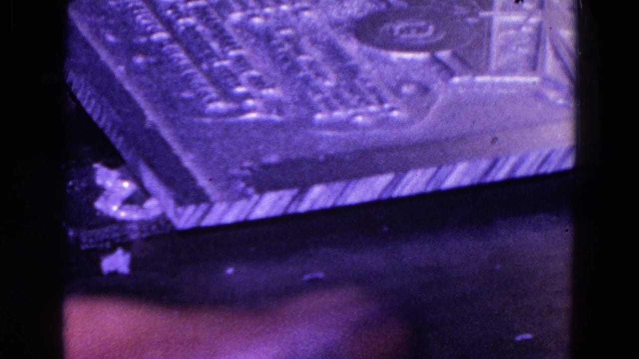 Textured rectangular mechanical object under purple light with a circular detail and striped lower edge.