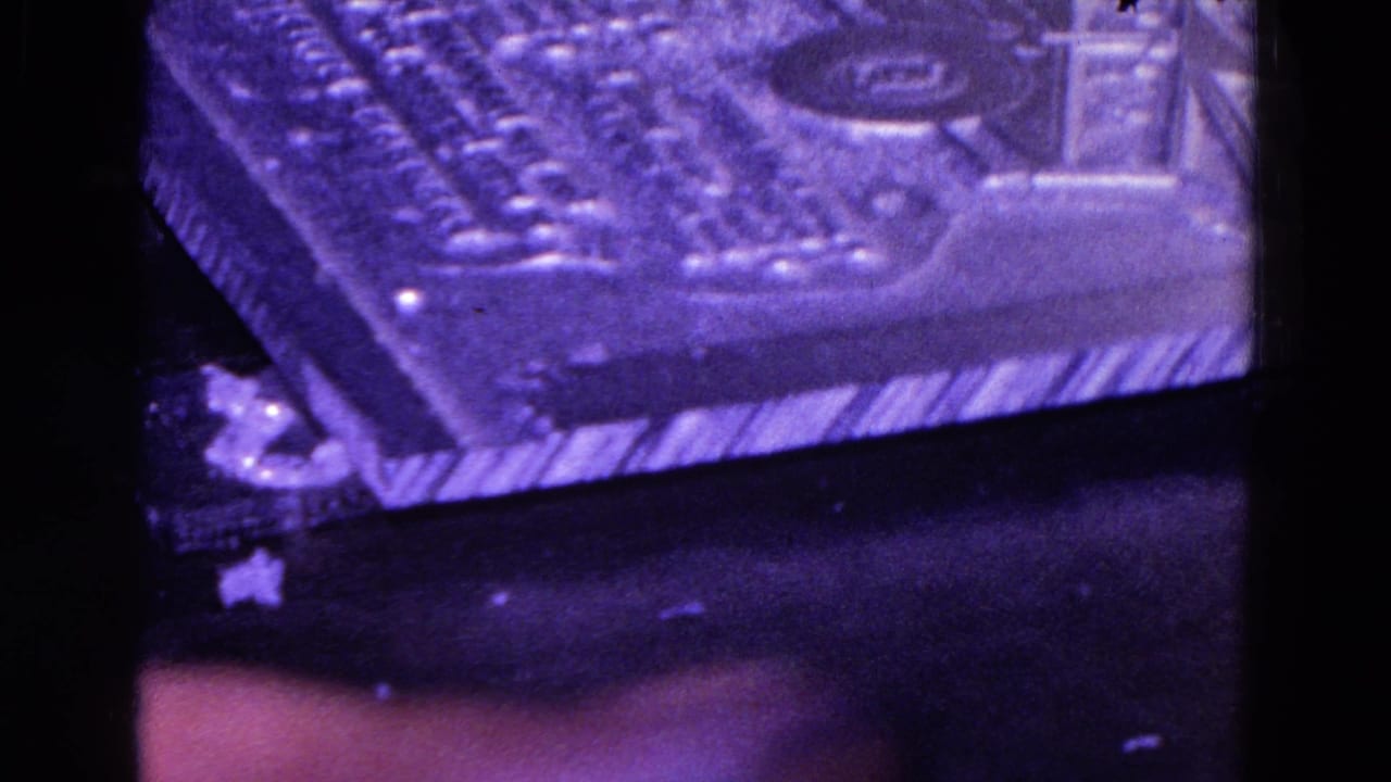 Similar close-up of a purple-lit rectangular object with raised texture and dark surroundings.
