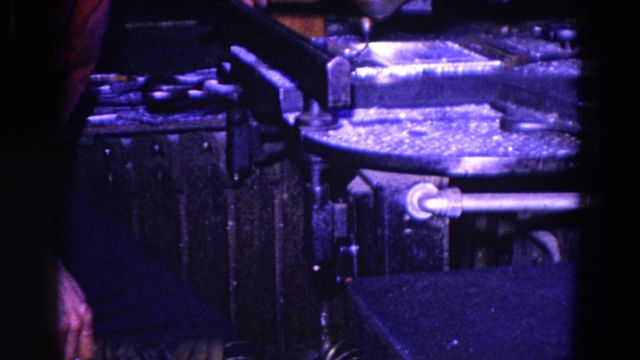 1967 8mm frame from Trenton showing a dark mechanic shop bench with metal parts, tools, and equipment in close view.
