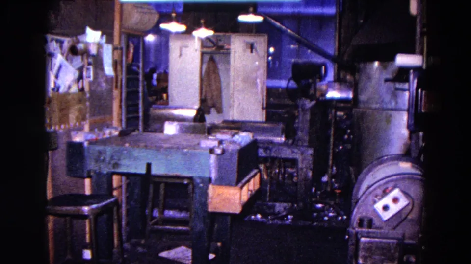 The workshop interior remains visible with benches, stools, machinery, and a coat on the door in the 1967 Trenton home-movie clip.