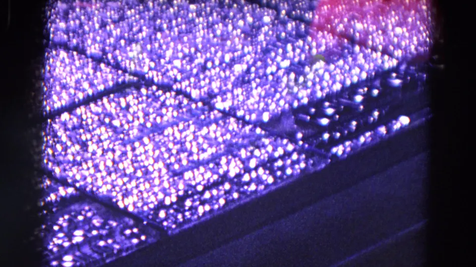 Close-up 8mm view of a dark machine surface, its textured top catching purple-blue reflected light.