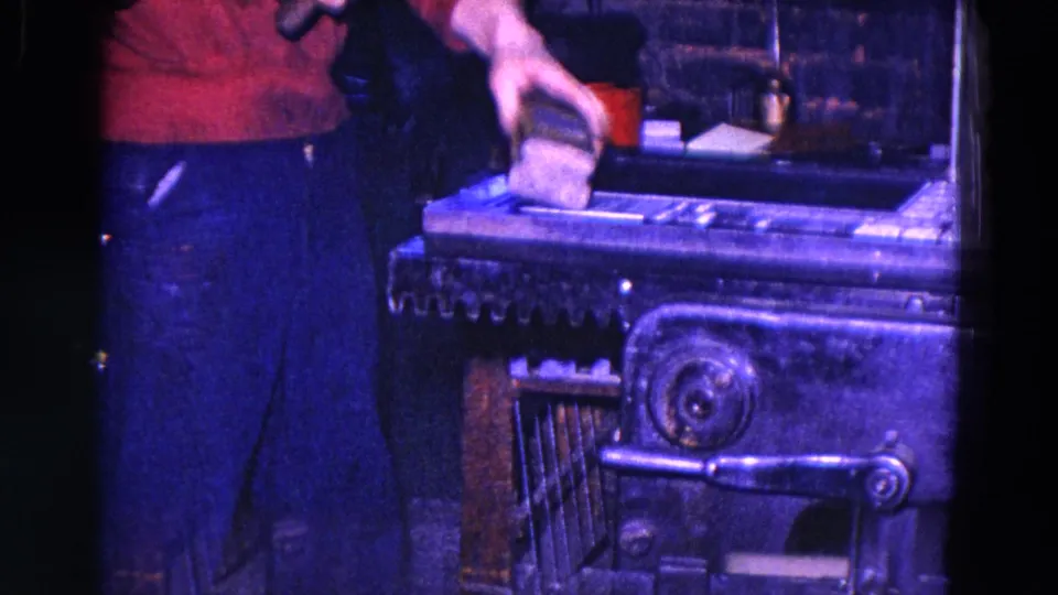 1967 Trenton 8mm frame with a worker's torso and hand holding material over an industrial printing press under blue-purple light.