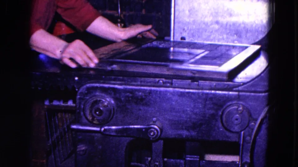 Close 1967 Trenton 8mm view of hands arranging paper or stock on an industrial press bed, with the machine body and lever below.