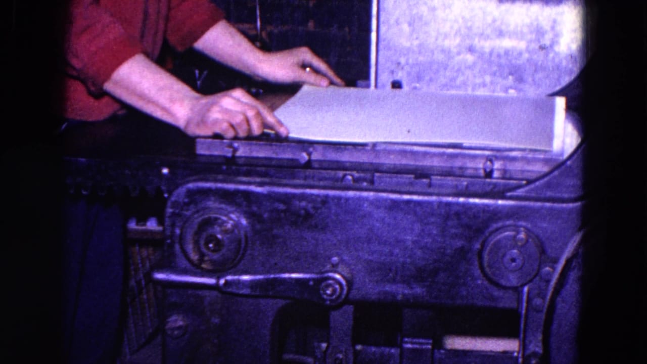 Worker hands position a large paper sheet on a dark industrial machine.