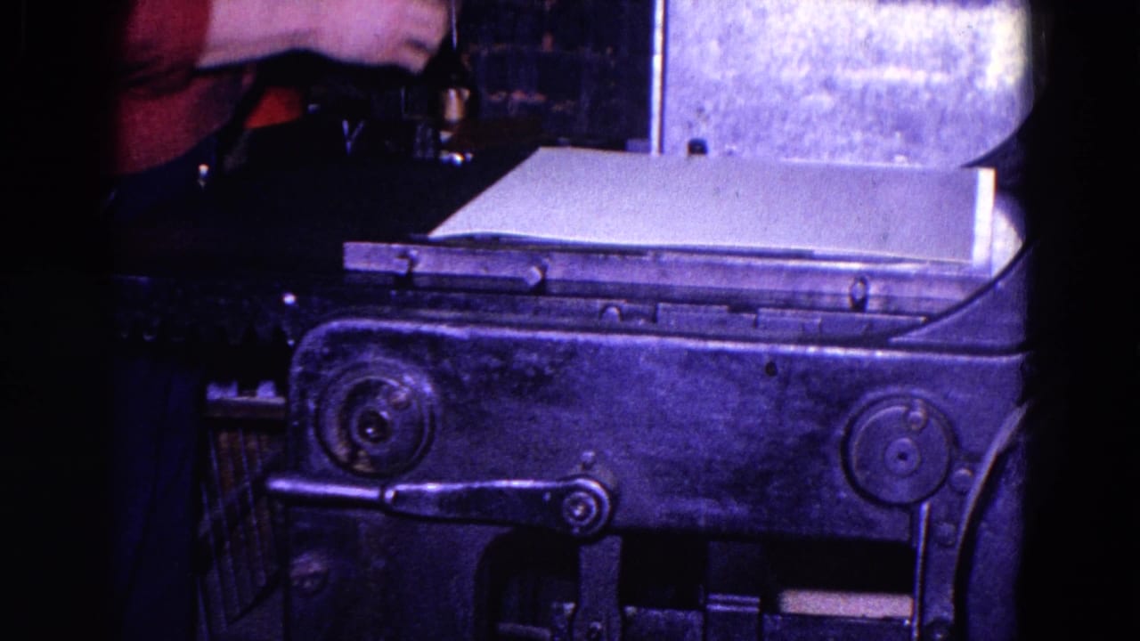 Large paper sheet rests on a metal machine while a worker stands partly out of frame.
