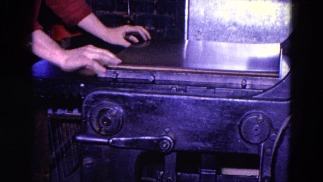 Worker's hands position material on the surface of a metal press.