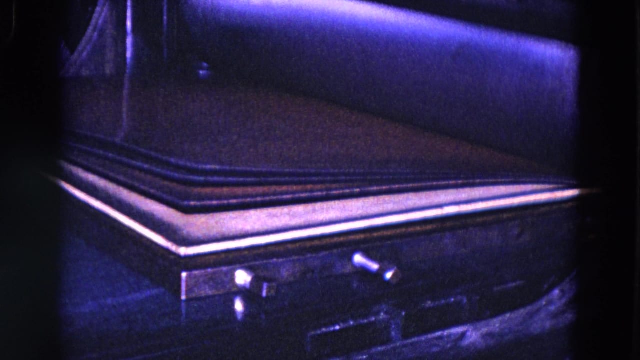 Close view of a dark book or cover on a machine bed with metal edging.