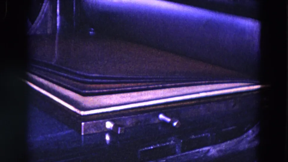 1967 Trenton 8mm close-up of a dark book or cover resting on an industrial machine bed with visible metal trim and blue-purple film color.