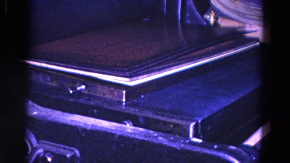 Close 8mm frame from Trenton, New Jersey, showing a dark book or cover moving through a press or conveyor area in a dim industrial setting.