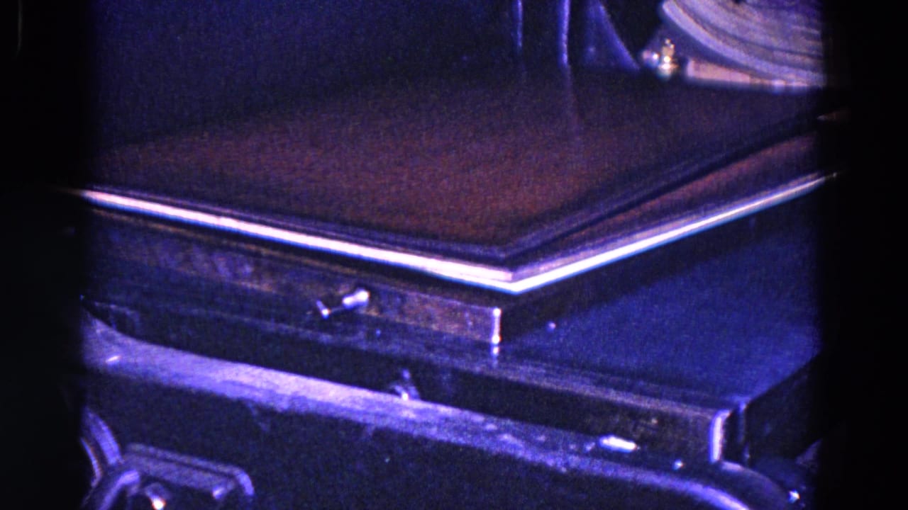 1967 Trenton close-up of book or cover material on a dark conveyor or press surface, with metal edges and strong blue-purple 8mm color shift.
