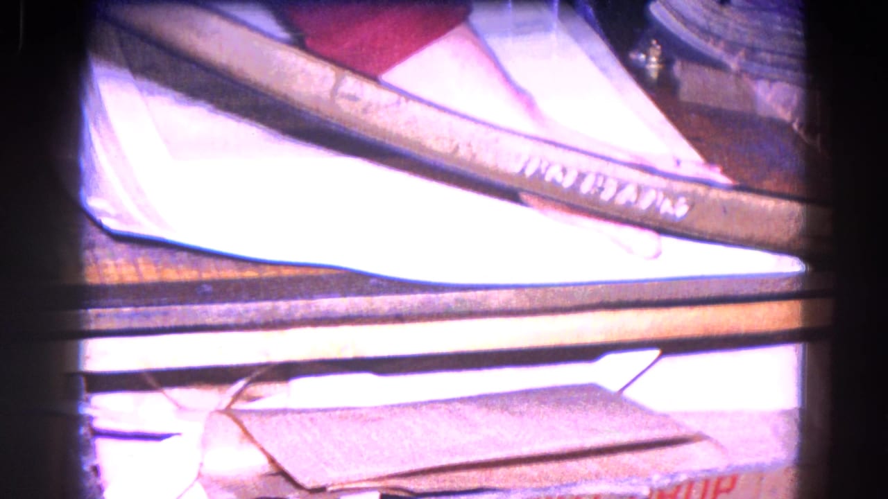 Final 8mm frame shows a hand or arm near light-colored book material and a marked band in the Trenton industrial close-up.