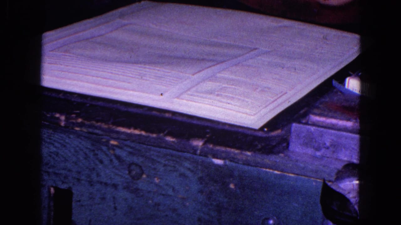 Close 8mm view of a large printed sheet or map on a cutter bed in the Trenton 1967 printing facility footage.