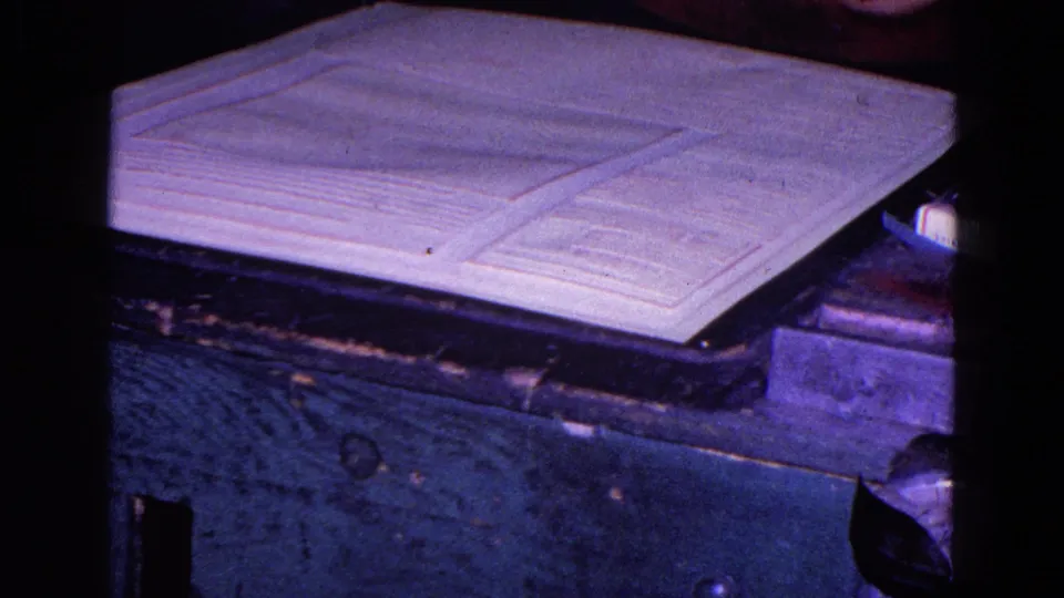 Close 8mm view of a large printed sheet or map on a cutter bed in the Trenton 1967 printing facility footage.