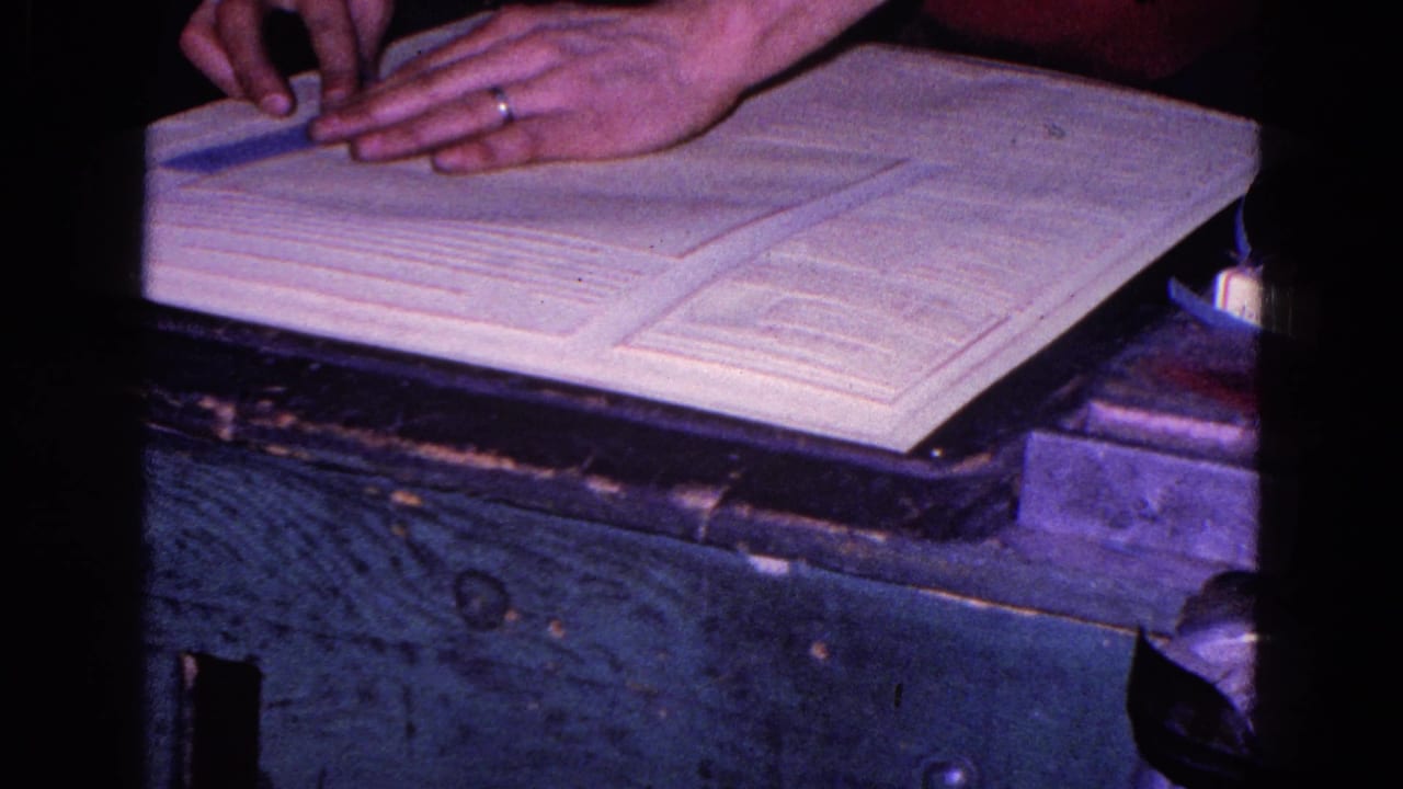 Hands, one wearing a ring, adjust a measuring tool or pin near the white fabric on a dark wooden surface in 1967 Trenton footage.