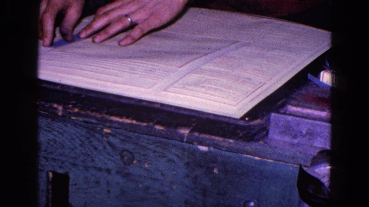 Hands near open papers on a wooden desk with dark film edges.