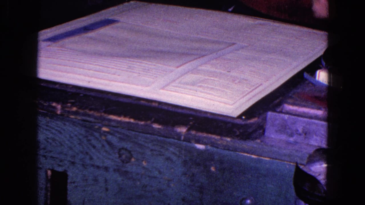 Open documents rest on a wooden desk in purple-blue 8mm footage, with a hand partly entering the frame.