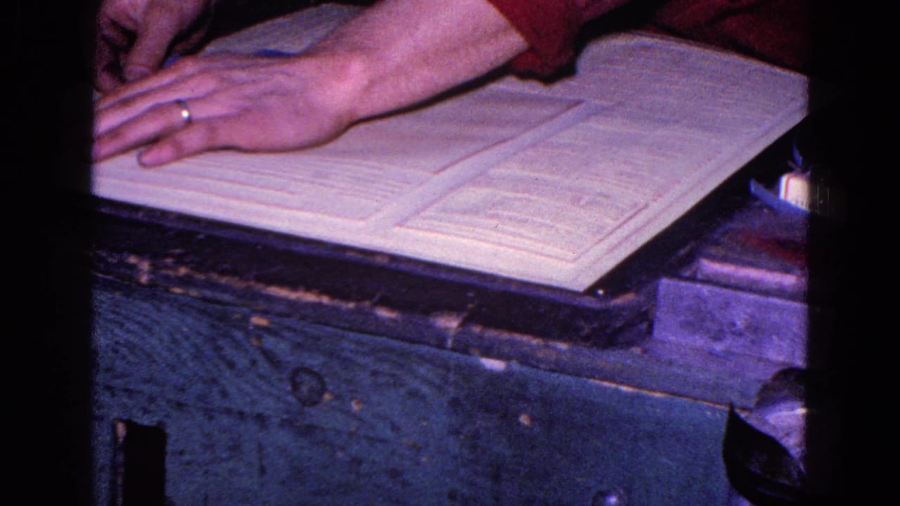 A ringed hand reaches across open paperwork on a wooden desk in 1967 Trenton home-movie footage.