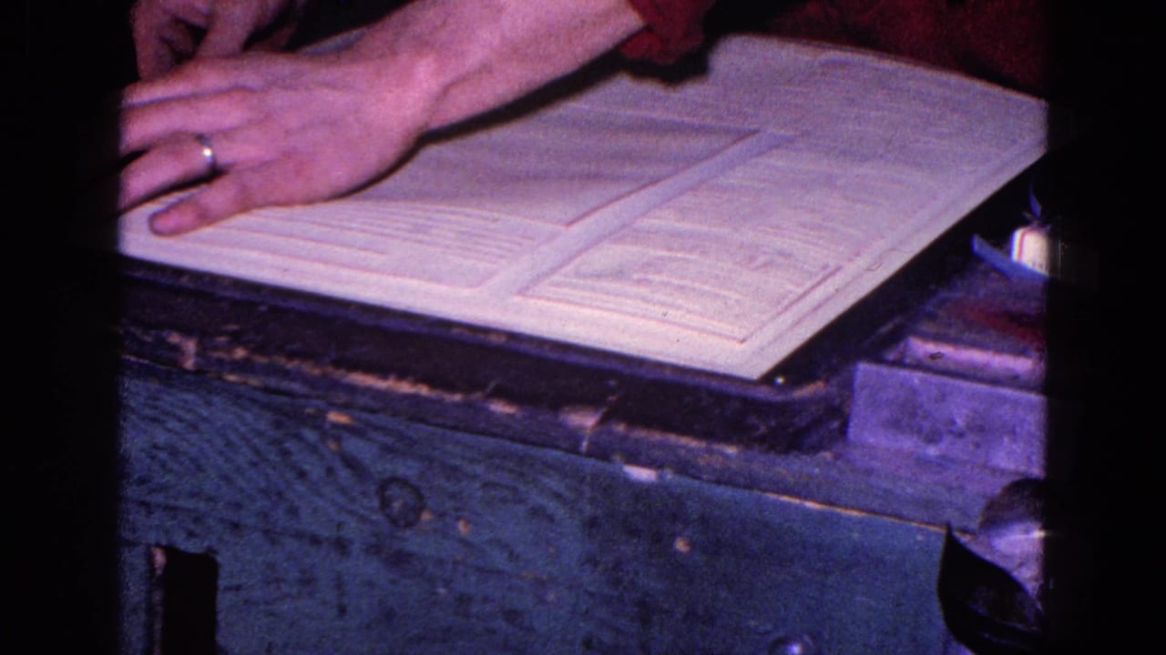Close 8mm frame of a ringed hand over open desk documents, consistent with paperwork or bookkeeping activity.