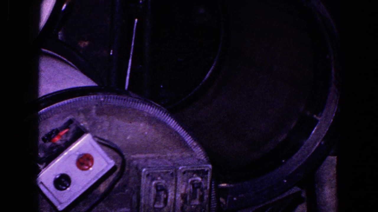 The final frame reveals a small control box with red and black buttons beside dark mechanical parts, possibly related to the work process.
