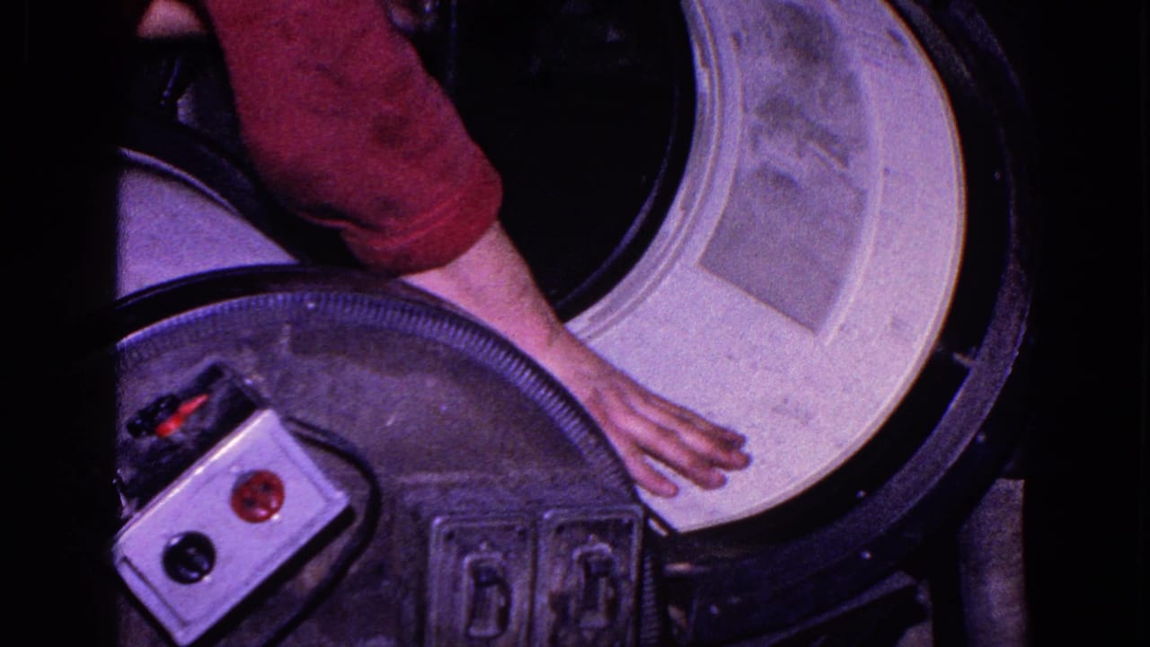 Close-up of a red-sleeved worker's arm smoothing or positioning paper inside a cylindrical press in Trenton, 1967.