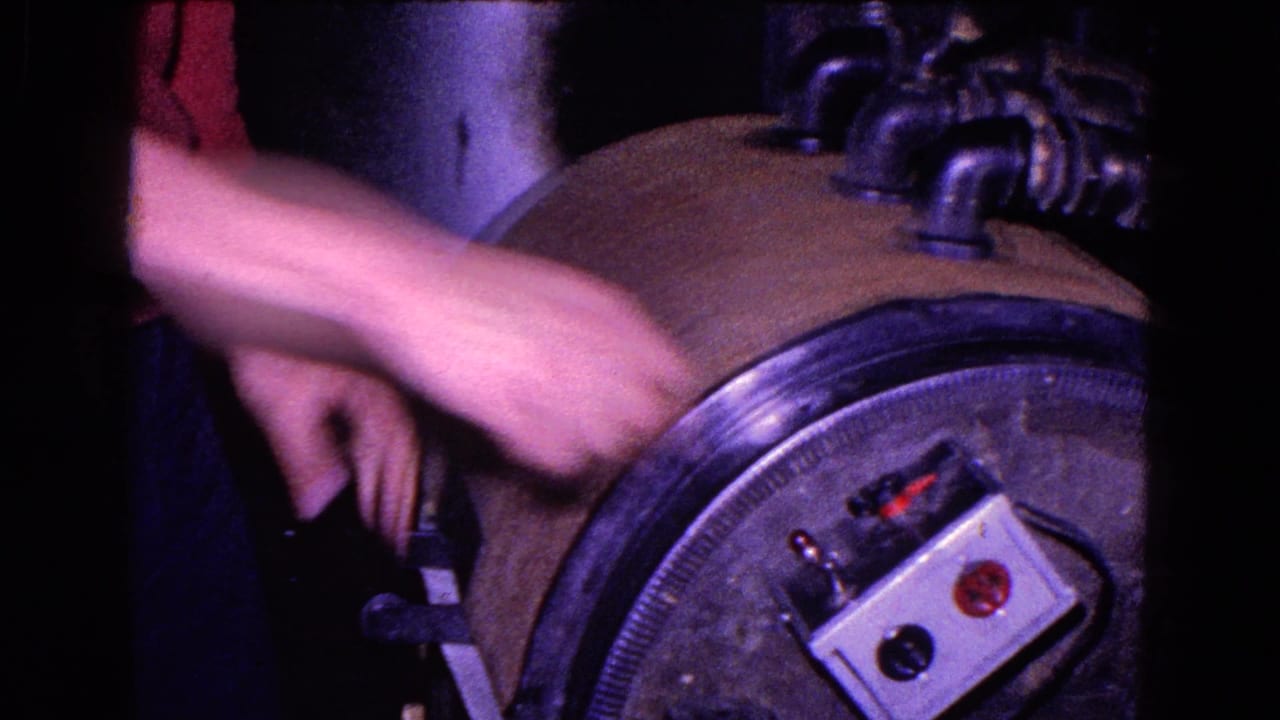 Close 1967 Trenton industrial view of hands near a rounded machine housing with a small control box and pipes.