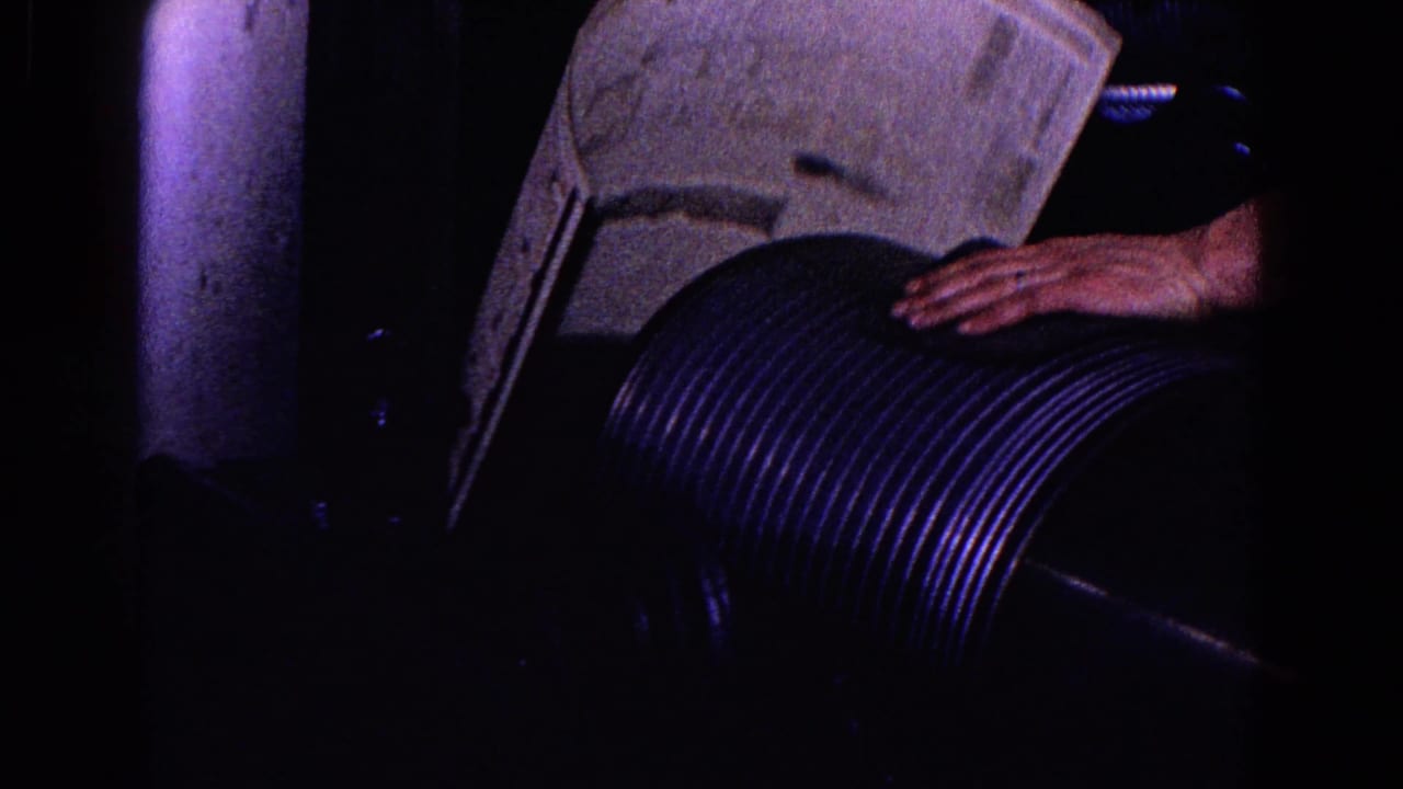 A hand rests on a ribbed cylindrical machine component beside a raised panel.
