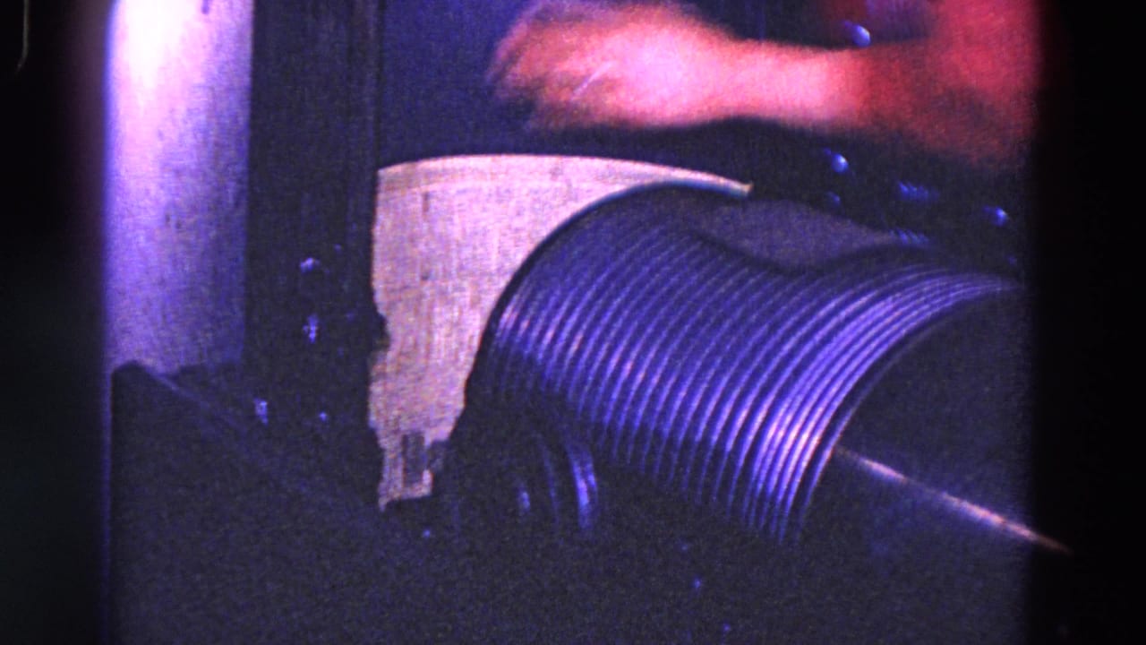 Worker's hand near a ribbed metal cylinder inside dark machinery with purple-blue light.