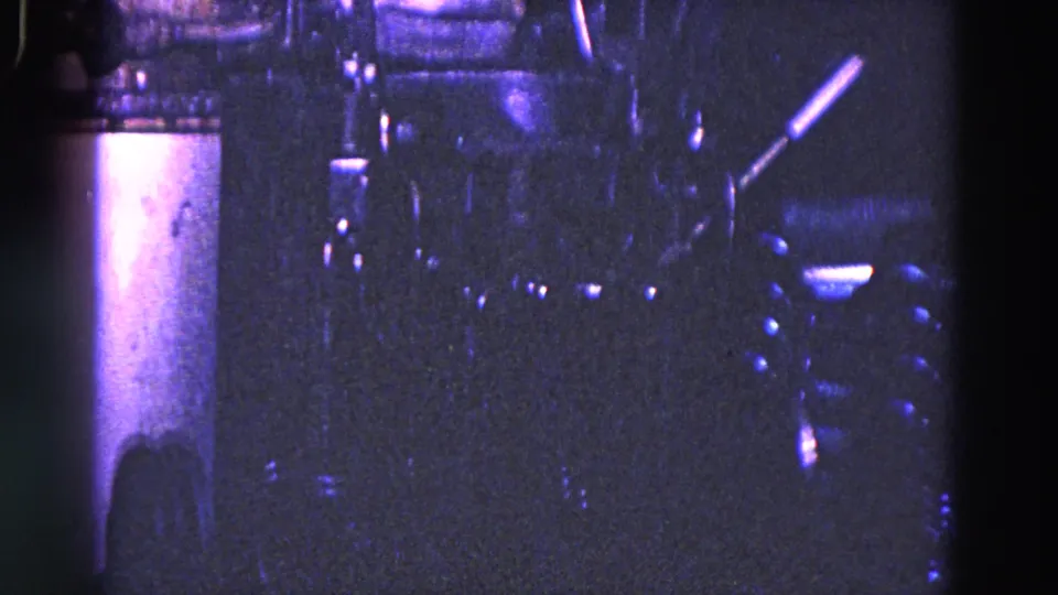 1967 industrial close-up showing vertical supports, small metal fittings, and a lever-like machine part in grainy purple-blue 8mm footage.