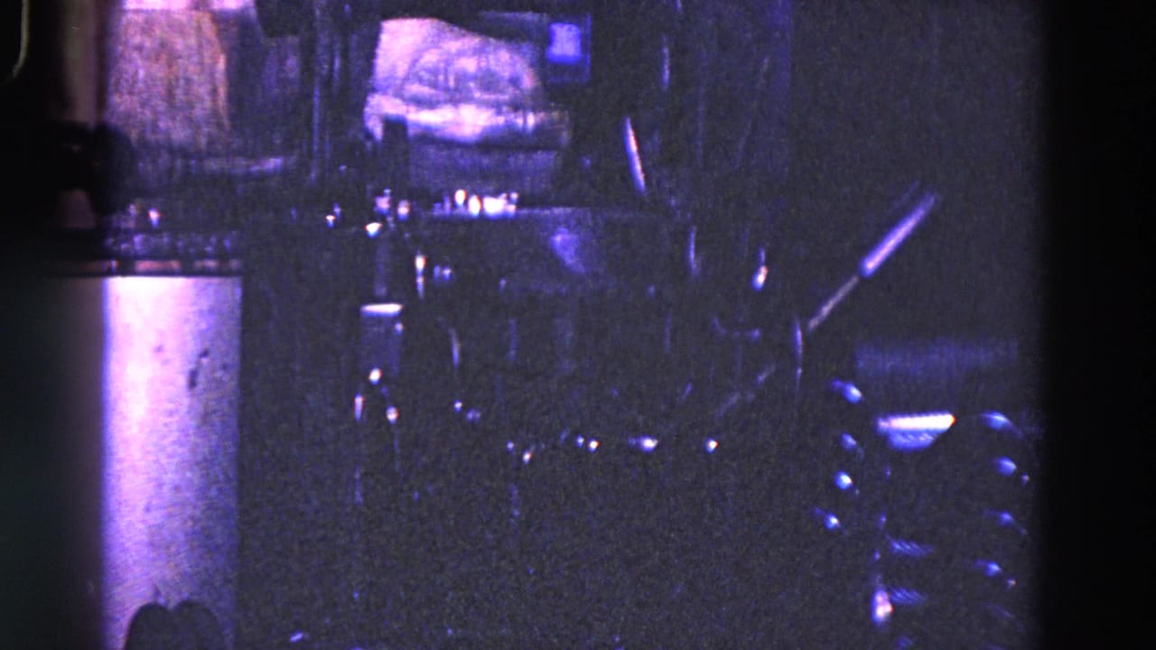 Dark bottling machinery and reflective equipment under purple-tinted factory light.