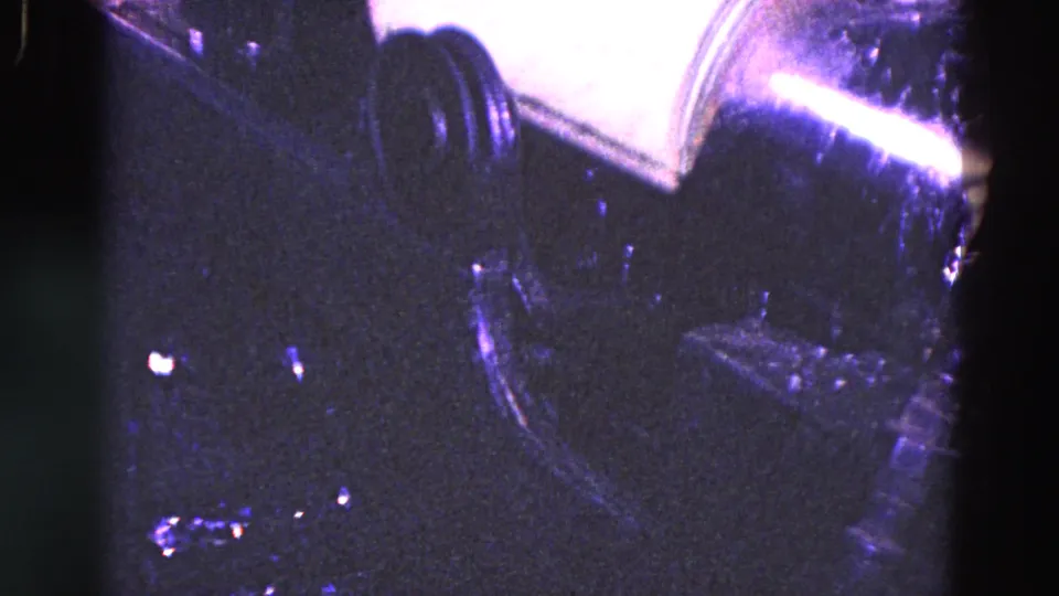 1967 Trenton bottling footage showing a cylindrical label roll or dispenser above dark industrial machinery.
