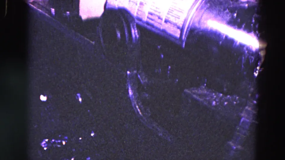 Close 8mm frame from Trenton showing a label roll or canister positioned over dark beverage bottling equipment.