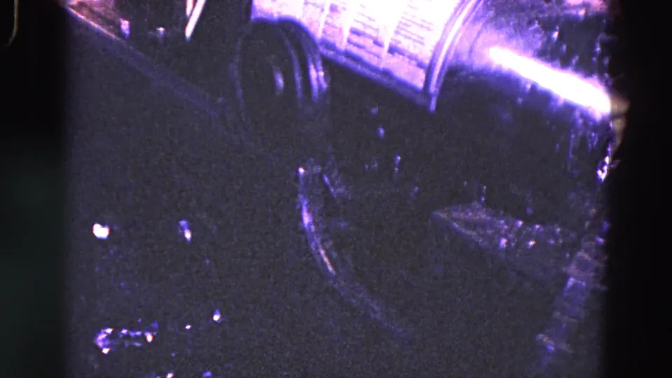 1967 Trenton industrial home-movie frame showing dark machine parts and a reflective metal cylinder in a close, grainy 8mm view.