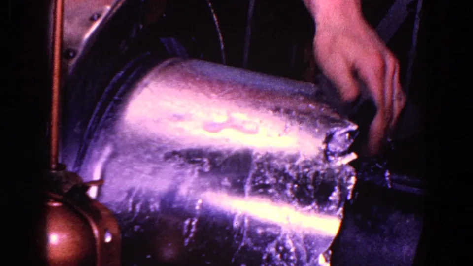 A worker's hand guides a shiny round metal tube into machinery in the 1967 Trenton industrial home-movie footage.