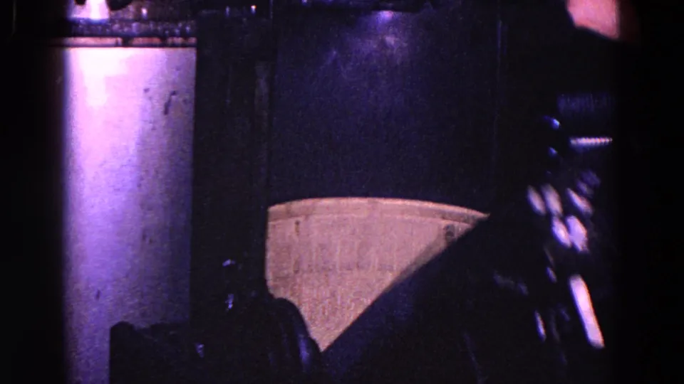 End frame of the Trenton industrial clip showing dark machinery, cylindrical metal parts, and a pale curved component in grainy 8mm color.
