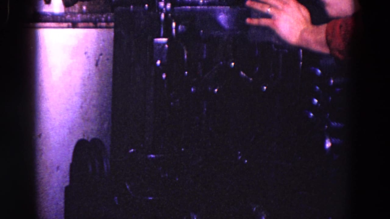1967 Trenton 8mm frame showing a worker's hand near dark industrial machinery under blue-purple light.