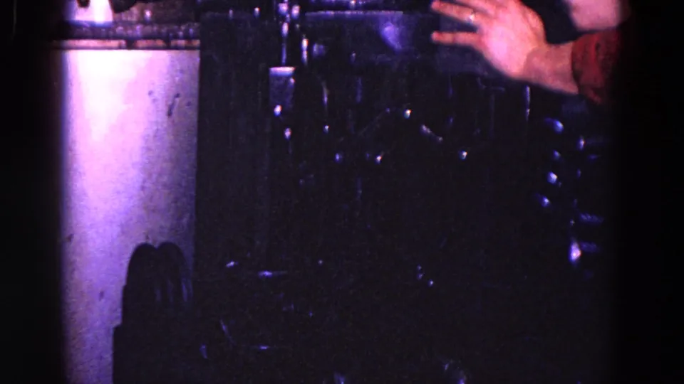1967 Trenton 8mm frame showing a worker's hand near dark industrial machinery under blue-purple light.