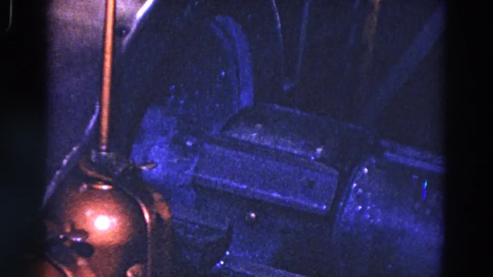 1967 Trenton 8mm frame showing a close view of blue-lit machinery, a copper-toned foreground component, and dark metal parts.