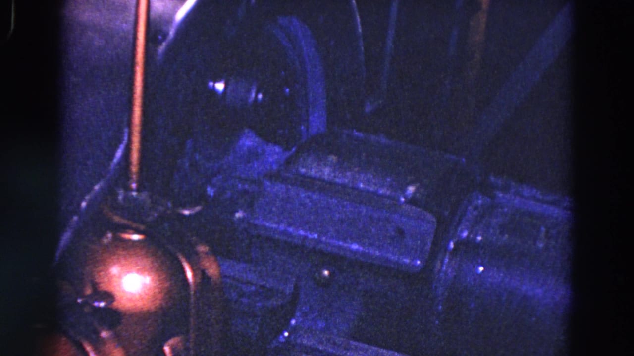 Dark industrial machine parts under blue light with a copper-toned component at left.