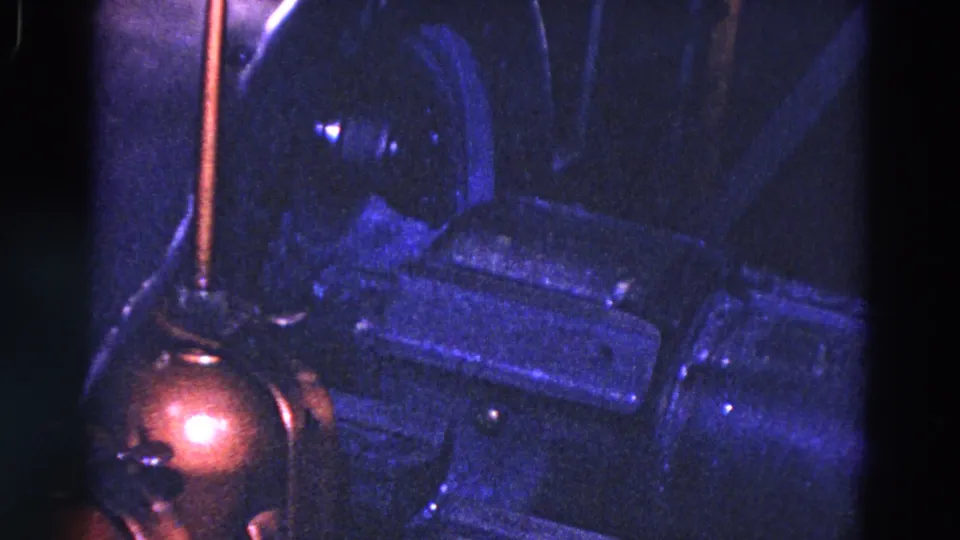 1967 Trenton 8mm frame with blue-purple lighting on industrial machine housings and a copper-colored part near the left edge.