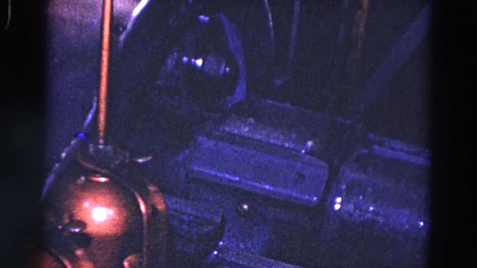 1967 Trenton 8mm frame showing a tight industrial machinery detail with blue light, a copper-colored foreground part, and metal housings.