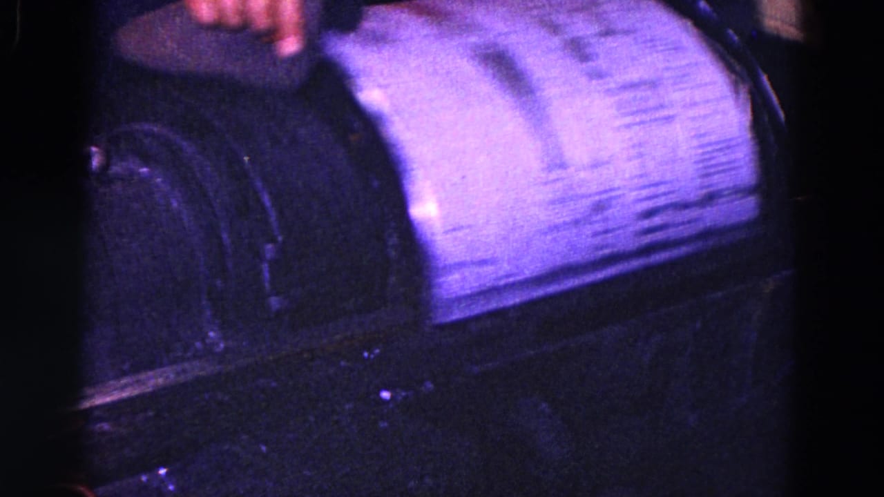 Close view of a dark industrial machine with a curved cylindrical section and a hand at the top edge.