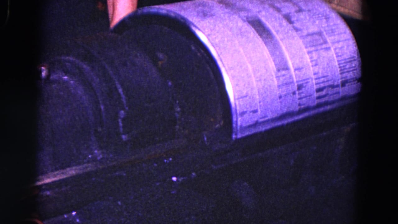 Close 8mm view of a Trenton industrial machine, with a dark housing and bright curved surface under purple-blue shop lighting.