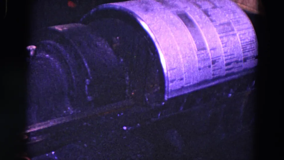 1967 8mm close-up of heavy machine parts in a Trenton shop, showing a dark housing and curved cylindrical surface.